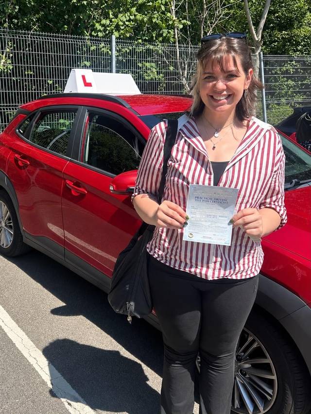 Learner 2 holding their driving test pass certificate beside a red training car