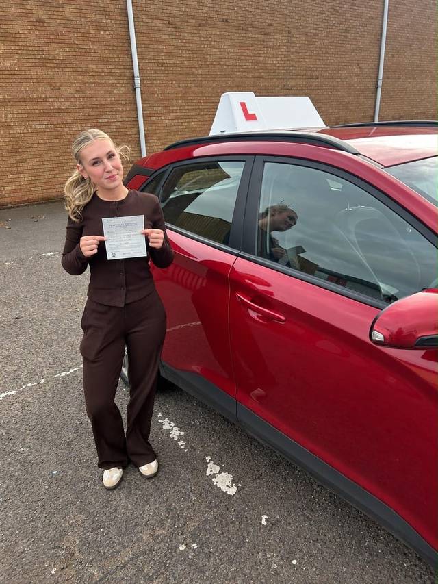 Learner 4 holding their driving test pass certificate beside a red training car